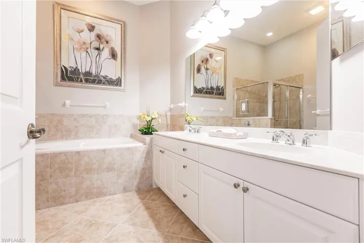 Full bath featuring double vanity, light tile patterned flooring, a stall shower, and tiled bath