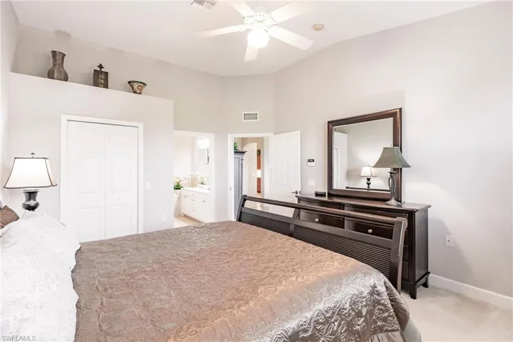 Bedroom featuring light carpet, a closet, ensuite bathroom, a ceiling fan, and lofted ceiling