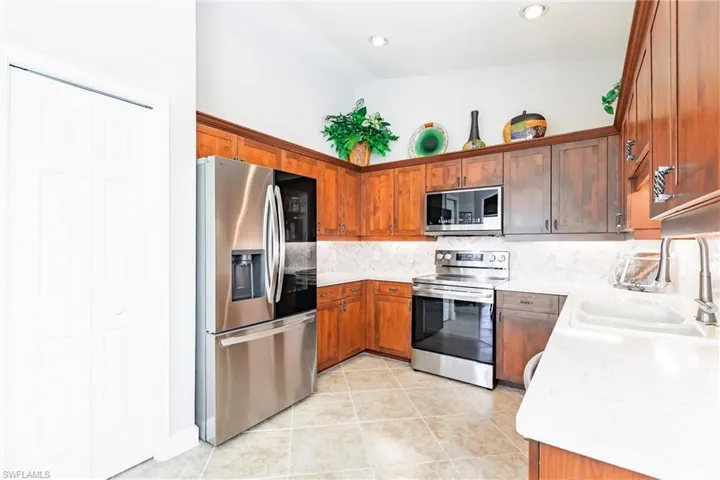 Kitchen with appliances with stainless steel finishes, backsplash, light tile patterned floors, light stone counters, and brown cabinetry