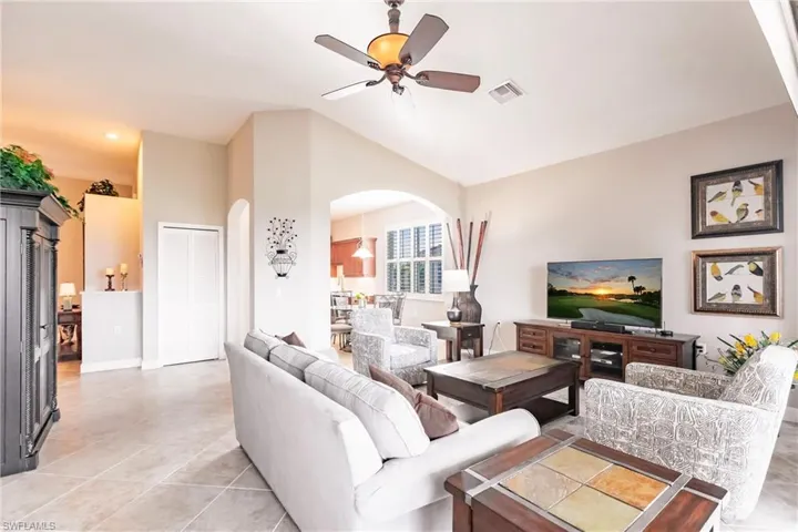 Living room with arched walkways, a ceiling fan, light tile patterned floors, and lofted ceiling
