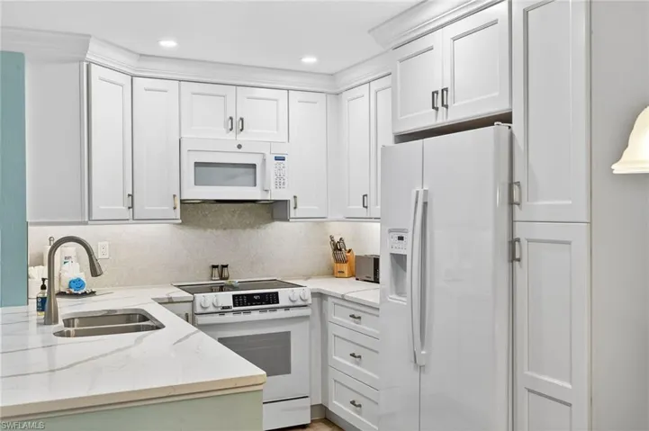 Kitchen featuring white appliances, light stone counters, white cabinets, and recessed lighting