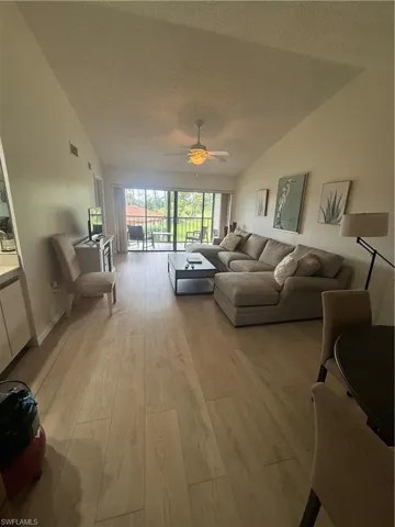 Living area featuring lofted ceiling, light wood-style flooring, a textured ceiling, and a ceiling fan