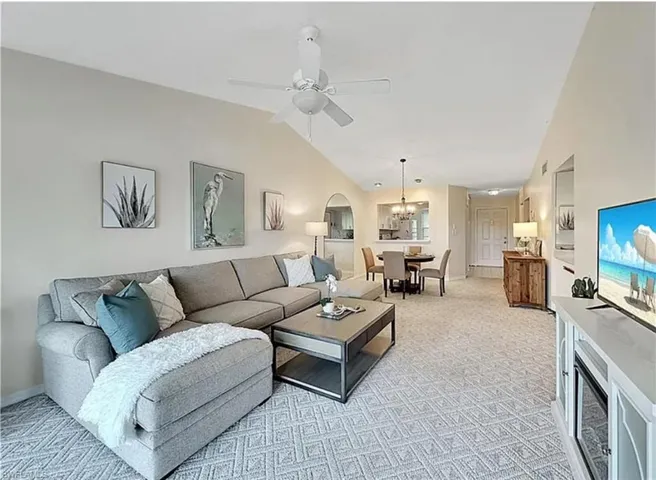 Living room with lofted ceiling, ceiling fan, light carpet, and a chandelier