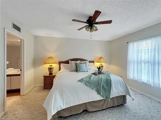 Bedroom with a textured ceiling, light colored carpet, connected bathroom, and ceiling fan