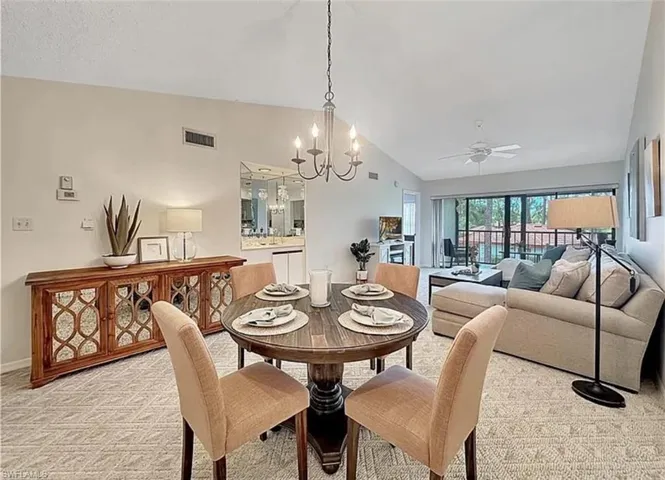 Dining area featuring vaulted ceiling, light carpet, a chandelier, and a ceiling fan
