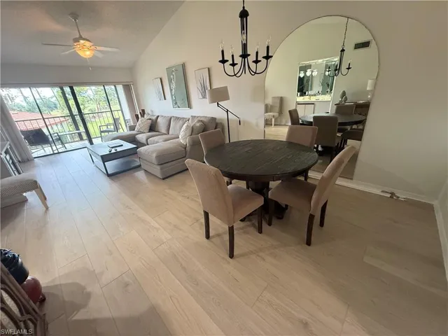 Dining room with light wood-style floors, a ceiling fan, a chandelier, high vaulted ceiling, and a textured ceiling
