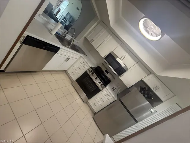 Kitchen with white cabinets, light tile patterned floors, stainless steel appliances, light countertops, and a towering ceiling