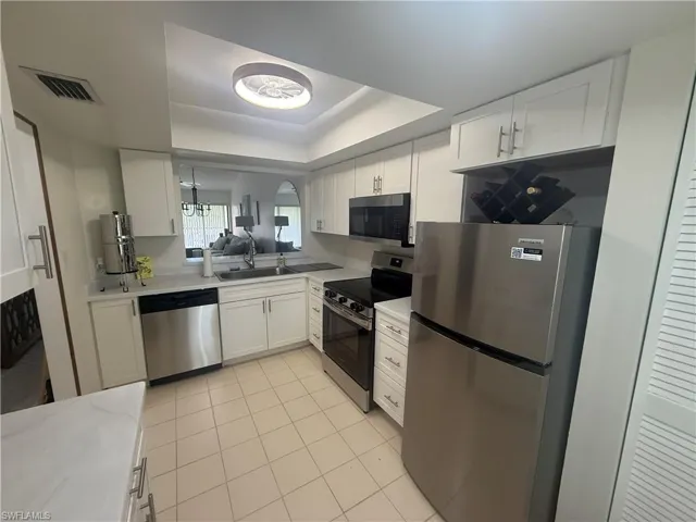 Kitchen with appliances with stainless steel finishes, white cabinetry, a tray ceiling, and light tile patterned floors