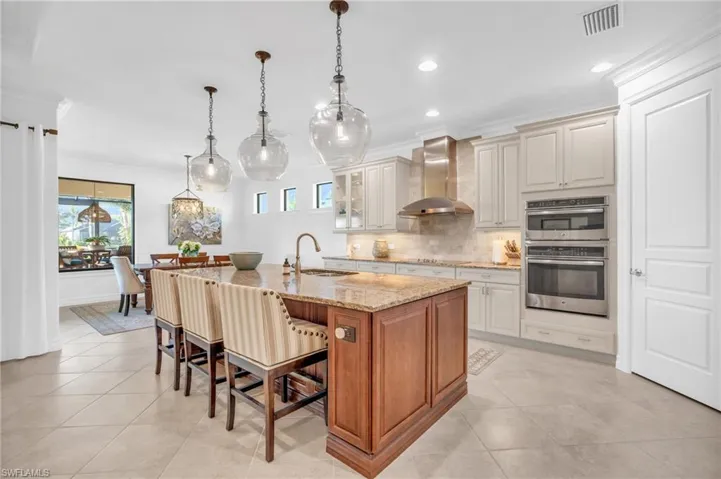 Kitchen with decorative light fixtures, sink, a kitchen island with sink, light stone countertops, and wall chimney exhaust hood