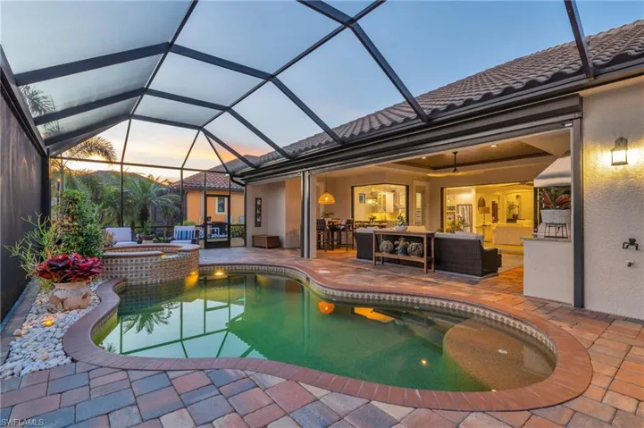 Pool at dusk featuring an in ground hot tub, an outdoor living space, a lanai, and a patio