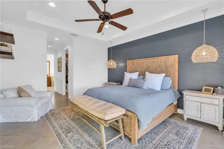 Bedroom featuring light tile patterned floors, crown molding, ceiling fan, ensuite bathroom, and a raised ceiling