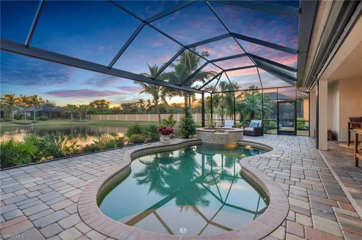 Pool at dusk featuring a patio area, a water view, and an in ground hot tub