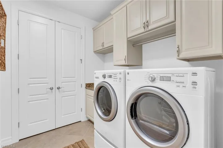Clothes washing area with cabinets, washer and dryer, and light tile patterned flooring