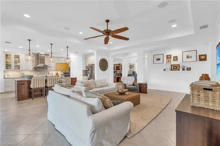 Living room with light tile patterned floors, ornamental molding, a raised ceiling, and ceiling fan