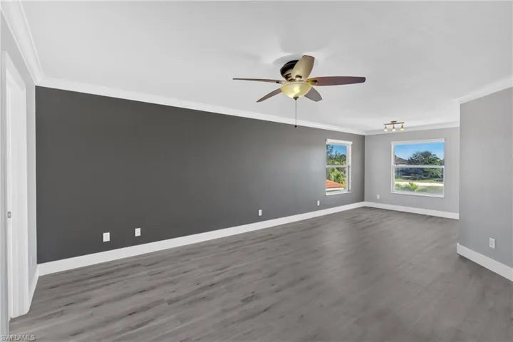 Unfurnished room with crown molding, a ceiling fan, and dark wood-style floors