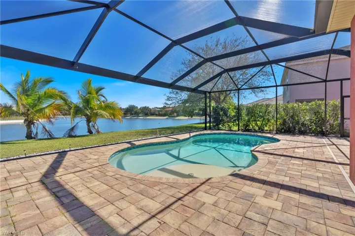 Outdoor pool with glass enclosure, a water view, a sunroom, and a patio area