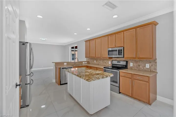 Kitchen with stainless steel appliances, a peninsula, crown molding, light stone countertops, and decorative backsplash