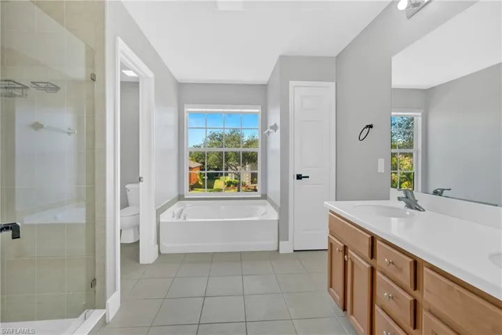 Full bath featuring double vanity, a bath, a stall shower, light tile patterned floors, and healthy amount of natural light