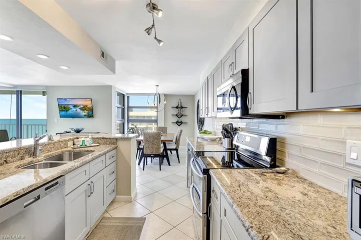 Kitchen with backsplash, rail lighting, light stone counters, stainless steel appliances, and sink