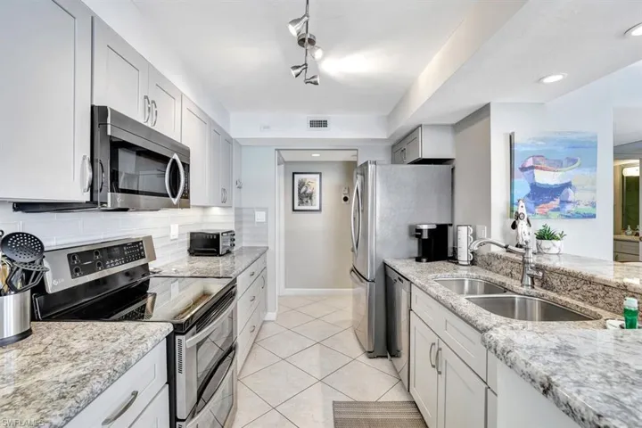 Kitchen with decorative backsplash, appliances with stainless steel finishes, light stone counters, and sink