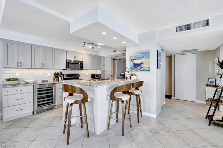 Kitchen featuring appliances with stainless steel finishes, light stone counters, gray cabinetry, beverage cooler, and a breakfast bar area