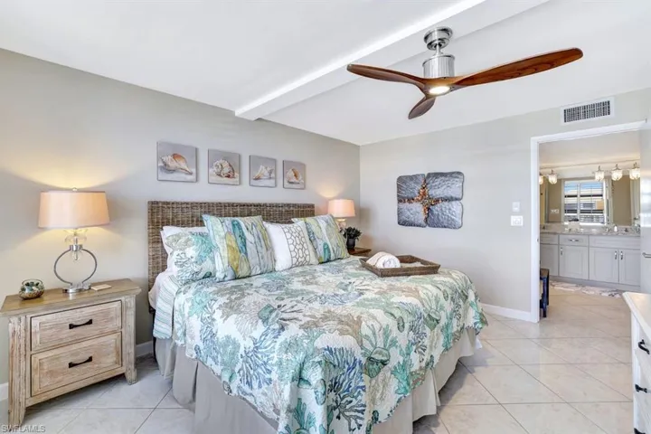 Bedroom featuring light tile patterned floors, connected bathroom, ceiling fan, and beam ceiling