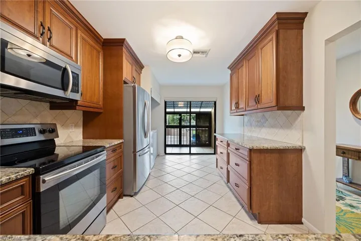 Kitchen featuring stainless steel appliances, wood finish cabinets, light stone countertops, and light tile patterned floors