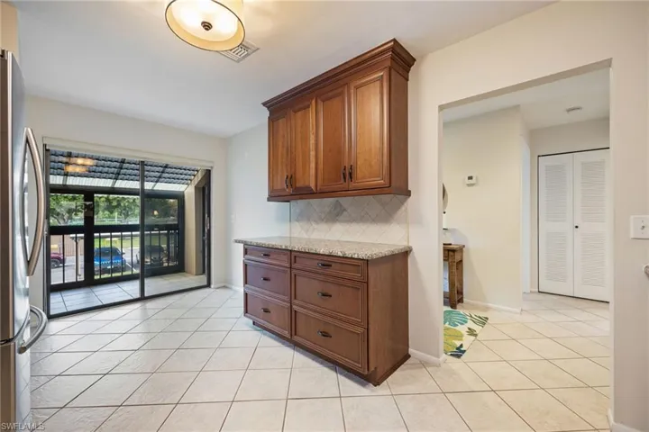 Kitchen featuring freestanding refrigerator, light tile patterned floors, decorative backsplash, light stone counters, and wood finish cabinetry