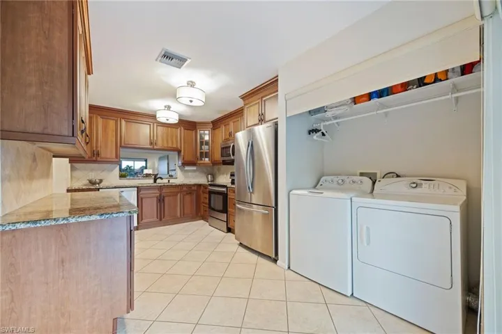 Kitchen with wood finish cabinets, light stone counters, stainless steel appliances, glass insert cabinets, and washing machine and dryer