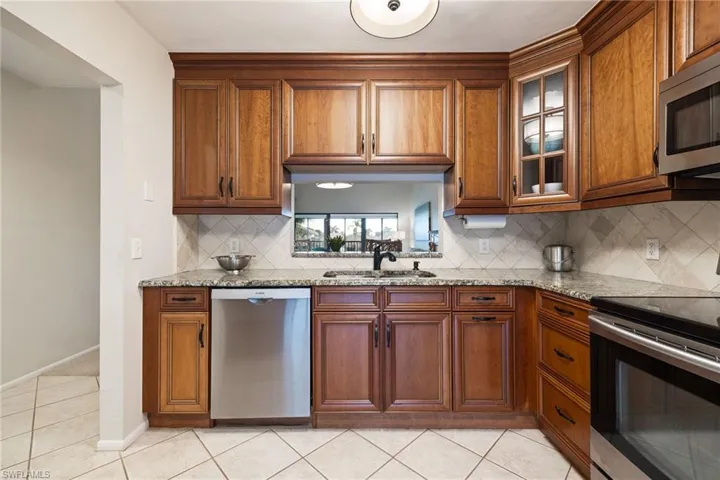 Kitchen with stainless steel appliances, light stone countertops, wood finish cabinets, and light tile patterned floors