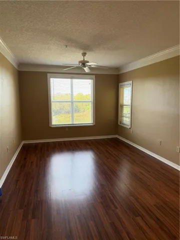 Empty room featuring dark wood-style flooring, a textured wall, a textured ceiling, crown molding, and a ceiling fan