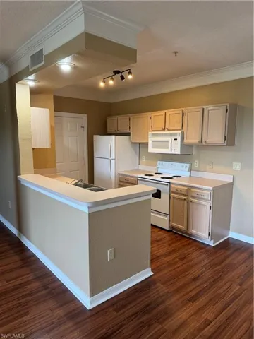 Kitchen featuring white appliances, light countertops, crown molding, dark wood-style flooring, and a peninsula