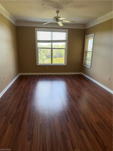 Empty room with dark wood-style floors, a textured ceiling, crown molding, ceiling fan, and a textured wall