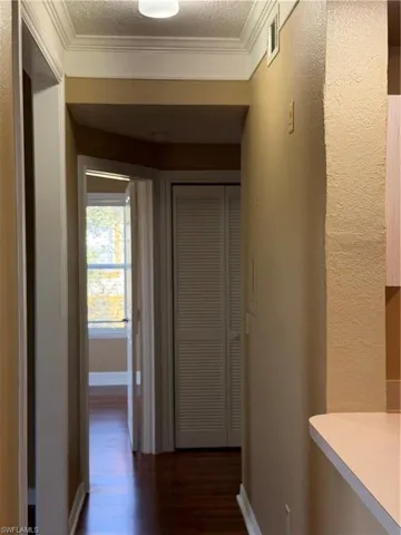 Hall featuring dark wood-type flooring, a textured ceiling, ornamental molding, and a textured wall