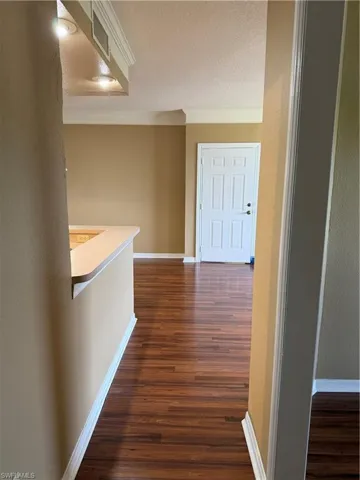 Corridor featuring dark wood-style flooring, a textured ceiling, and ornamental molding
