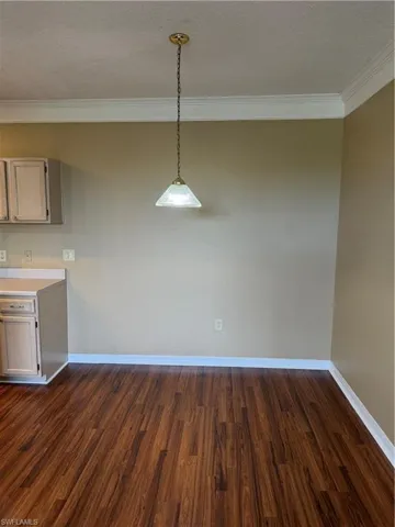 Unfurnished dining area with ornamental molding, dark wood-style flooring, and a textured ceiling