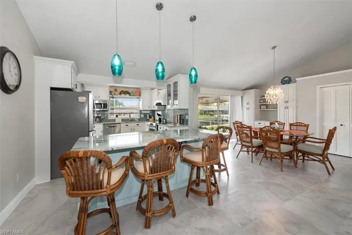 Kitchen featuring lofted ceiling, appliances with stainless steel finishes, light stone counters, a chandelier, and white cabinetry