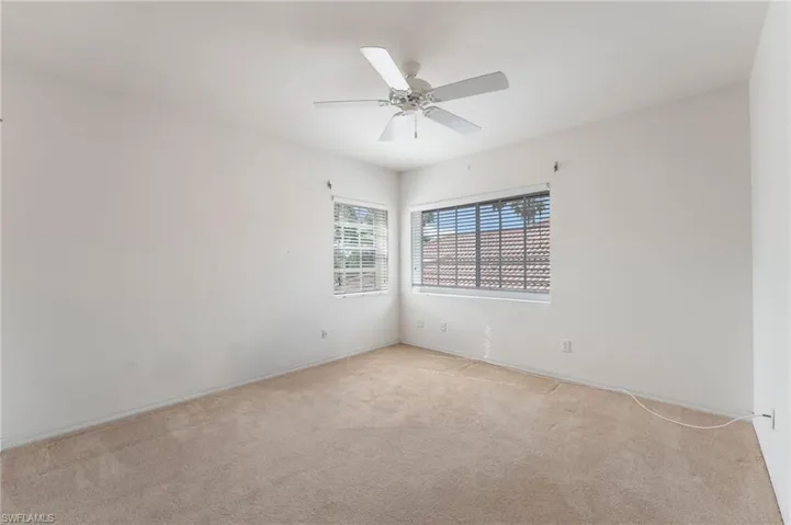 Carpeted room featuring multiple windows with blinds, a ceiling fan with integrated lighting, and neutral wall finishes