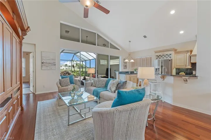 Expansive living area featuring vaulted ceilings with high transom windows, wood-finish flooring, and a built-in entertainment center