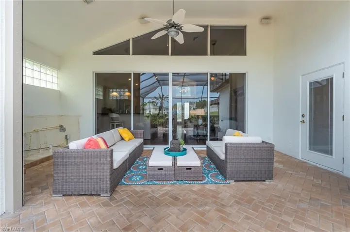 Spacious screened patio featuring herringbone-patterned brick pavers, a high vaulted ceiling with a ceiling fan, large glass sliding doors, and transom windows for abundant light