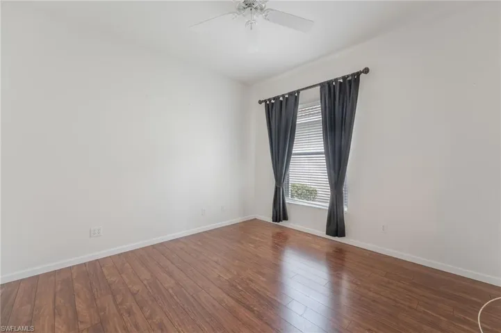 Expansive room featuring wood-finish flooring, white walls, and a white ceiling fan