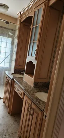 Full bath with double vanity, a tile shower, and light tile patterned floors