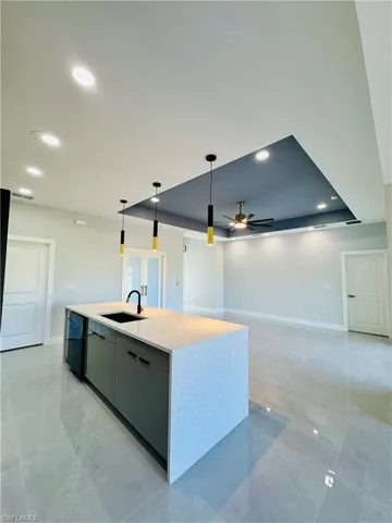 Kitchen featuring a tray ceiling, recessed lighting, a kitchen island with sink, modern cabinets, and pendant lighting