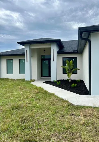 Doorway to property featuring stucco siding, a lawn, and roof with shingles