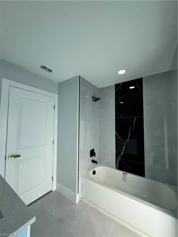 Bathroom featuring bathtub / shower combination, vanity, marble finish flooring, and recessed lighting