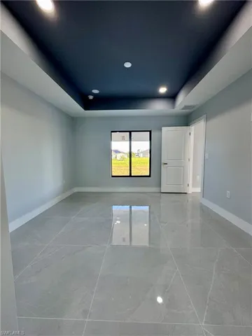 Empty room featuring a raised ceiling, recessed lighting, and marble finish floors