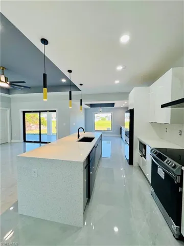 Kitchen featuring modern cabinets, stainless steel range with electric stovetop, white cabinetry, decorative light fixtures, and healthy amount of natural light