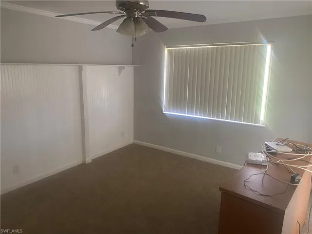 Unfurnished room featuring crown molding, dark colored carpet, and a ceiling fan