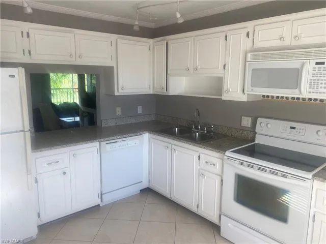 Kitchen with white appliances, white cabinetry, light tile patterned flooring, and crown molding