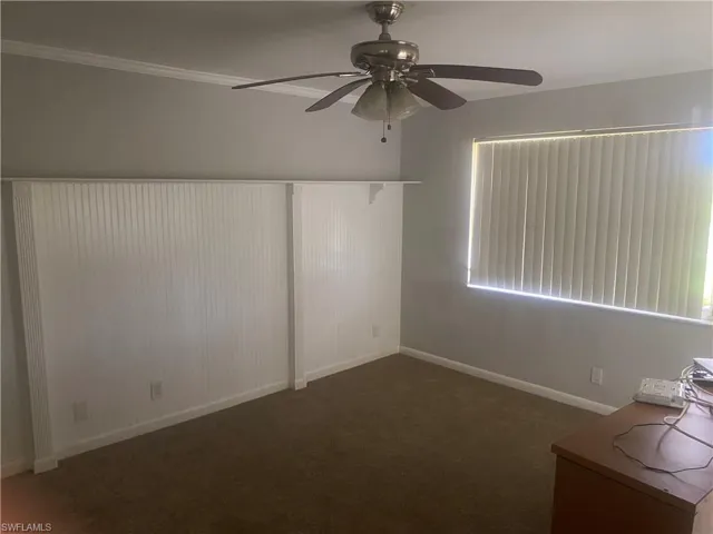 Spare room with a ceiling fan, dark carpet, and ornamental molding